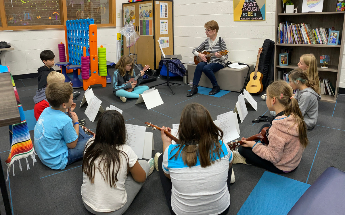A group of children sit in a circle as they learn to play the ukelele
